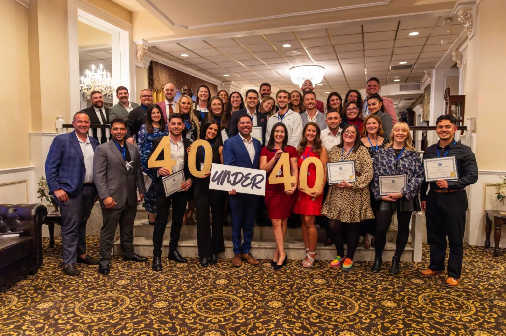 40 Under 40 honorees posing together at the awards ceremony, holding certificates and large 40 Under 40 signs