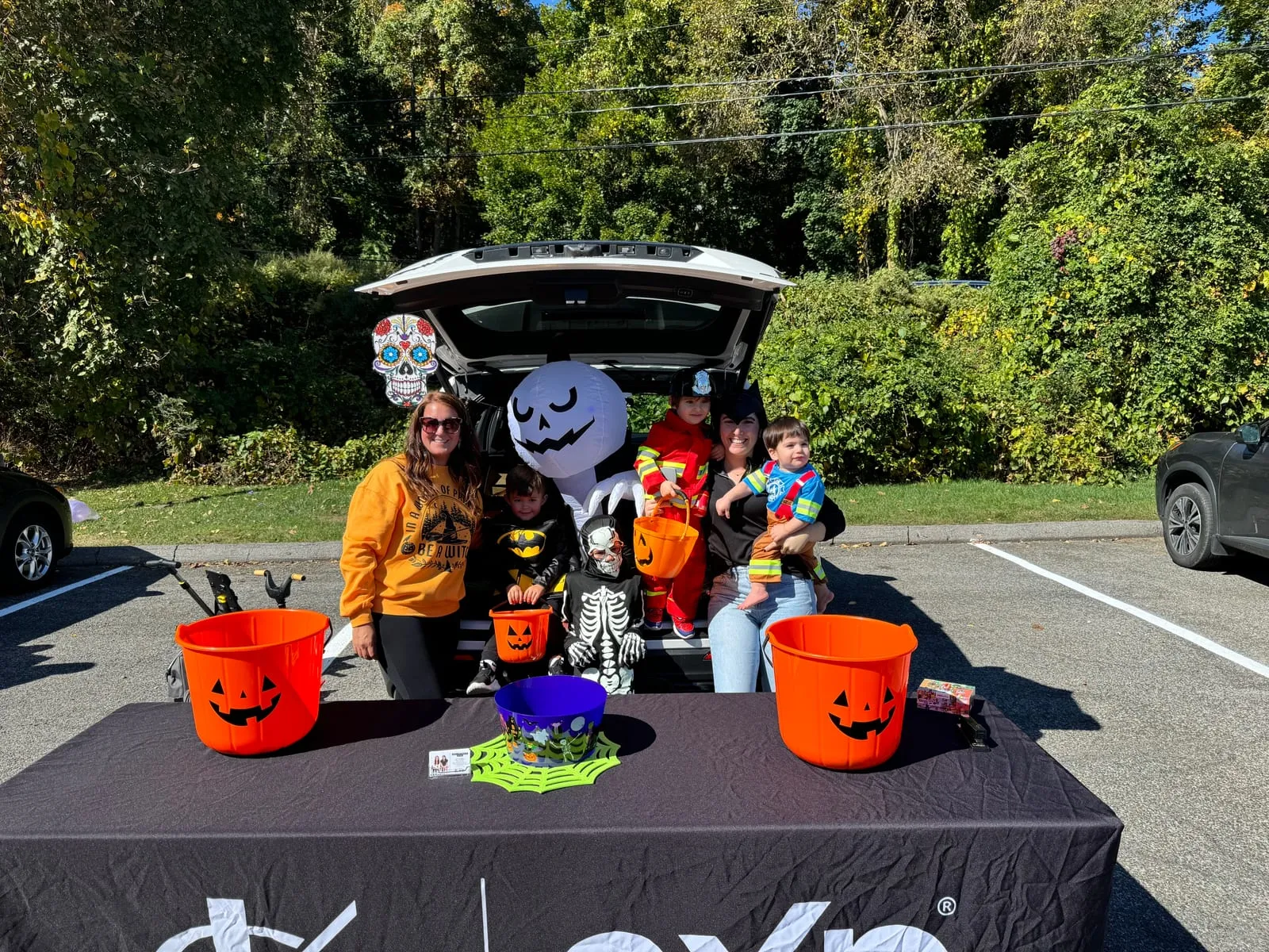 Team members and kids in costume at a Halloween-decorated trunk with pumpkin buckets